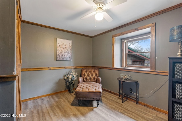 living area featuring wood finished floors, crown molding, baseboards, and a ceiling fan
