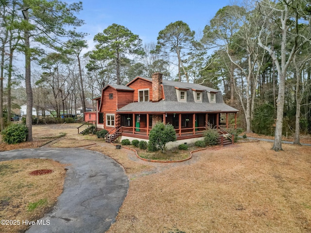 view of front of house featuring a chimney, roof with shingles, a porch, and driveway