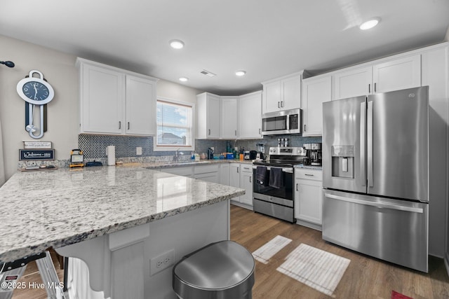 kitchen featuring white cabinetry, kitchen peninsula, appliances with stainless steel finishes, light stone counters, and a breakfast bar