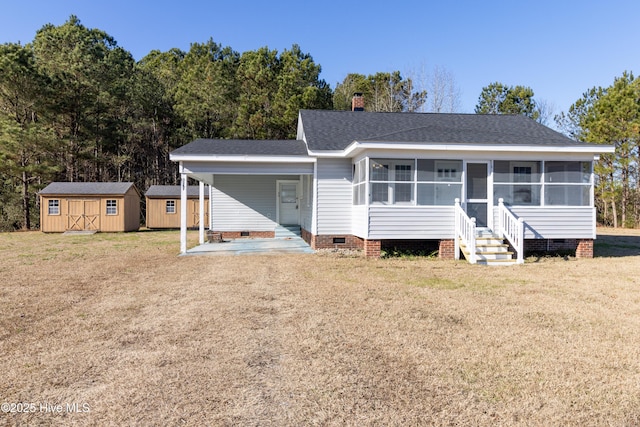 view of front of property featuring a sunroom, a front lawn, and a storage shed