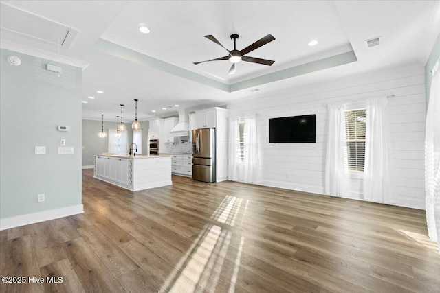 unfurnished living room featuring light hardwood / wood-style floors, sink, a raised ceiling, and ceiling fan