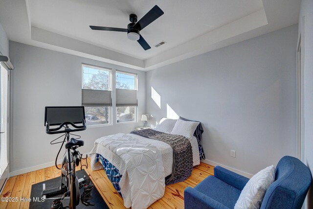 bedroom with ceiling fan, a tray ceiling, and light hardwood / wood-style flooring