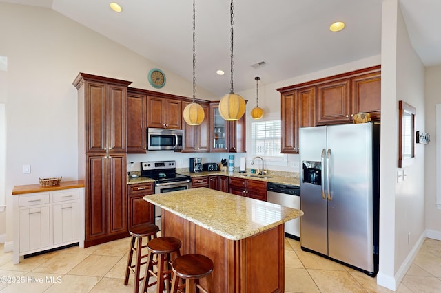 kitchen featuring pendant lighting, a center island, lofted ceiling, light stone countertops, and stainless steel appliances