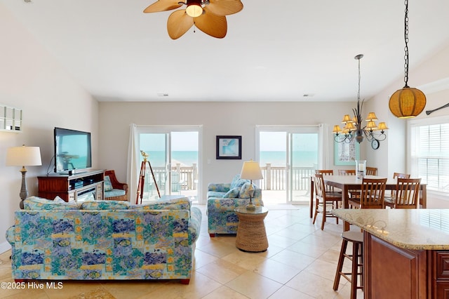 living room featuring light tile patterned floors, ceiling fan with notable chandelier, a water view, and a healthy amount of sunlight