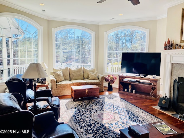 living room with a tiled fireplace, hardwood / wood-style floors, ornamental molding, and a healthy amount of sunlight