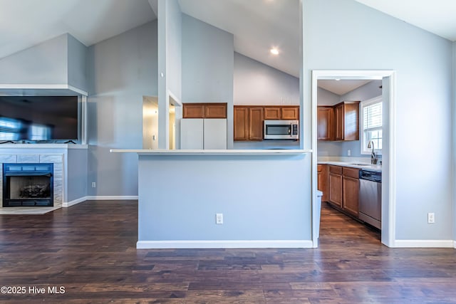 kitchen with a kitchen island, appliances with stainless steel finishes, sink, a tiled fireplace, and dark wood-type flooring