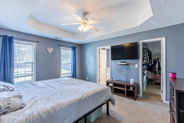 carpeted bedroom with a spacious closet, ceiling fan, a tray ceiling, ensuite bath, and a closet