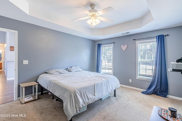 bedroom with a raised ceiling, light carpet, and multiple windows