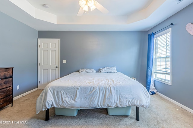 carpeted bedroom with ceiling fan and a raised ceiling