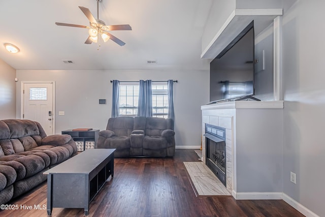 living room featuring a tiled fireplace, dark hardwood / wood-style floors, and ceiling fan