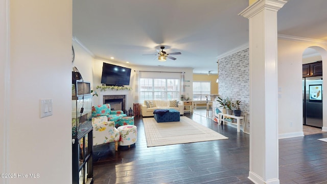 living room with crown molding, ceiling fan, a fireplace, and dark wood-type flooring