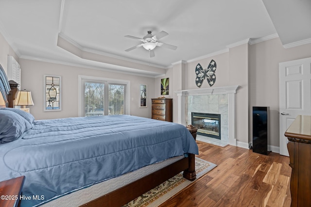 bedroom with a tile fireplace, hardwood / wood-style flooring, ornamental molding, ceiling fan, and a raised ceiling