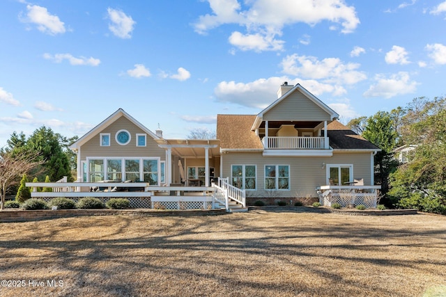 rear view of property featuring a balcony, a yard, and a deck