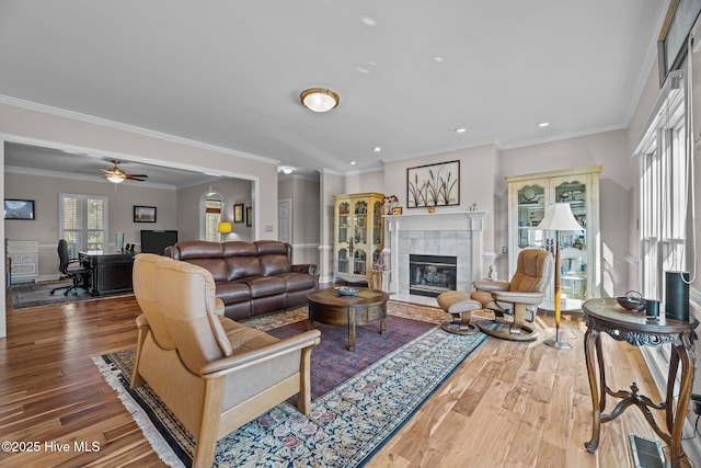 living room featuring a tiled fireplace, ornamental molding, hardwood / wood-style floors, and ceiling fan