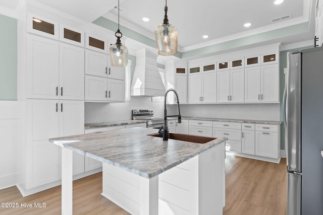 kitchen featuring custom exhaust hood, stainless steel appliances, a kitchen island with sink, white cabinets, and sink