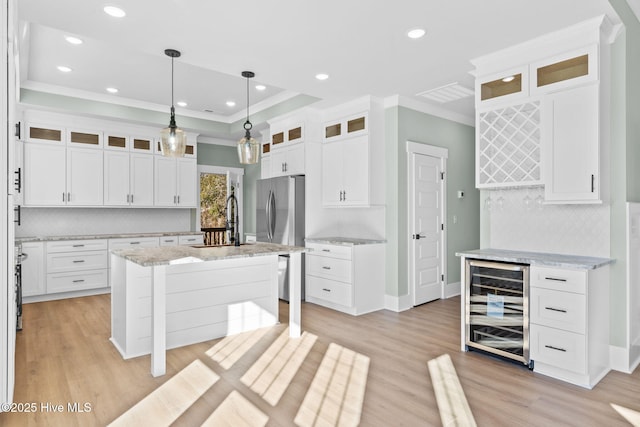 kitchen with pendant lighting, white cabinetry, a kitchen island with sink, and wine cooler