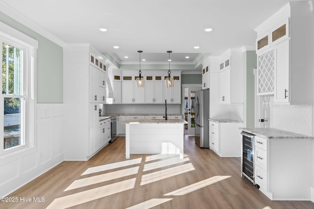 kitchen with stainless steel appliances, white cabinetry, a kitchen island with sink, and beverage cooler