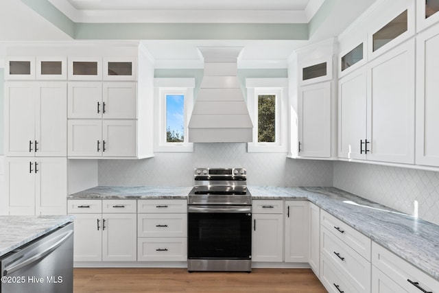 kitchen featuring stainless steel appliances, light stone countertops, custom range hood, decorative backsplash, and white cabinetry