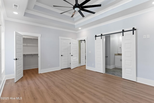 unfurnished bedroom featuring light hardwood / wood-style flooring, connected bathroom, a barn door, a tray ceiling, and ceiling fan