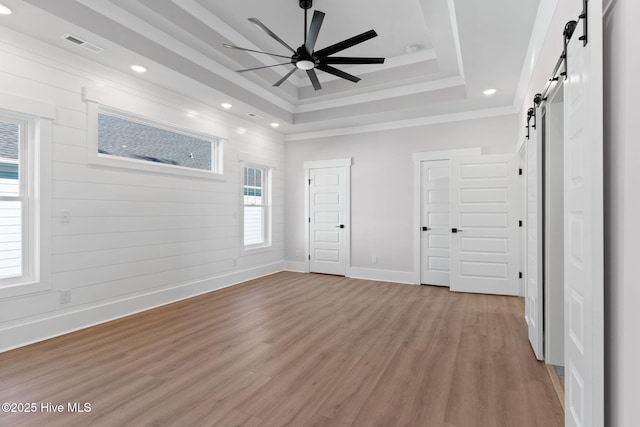 spare room featuring a raised ceiling, ceiling fan, a barn door, and light hardwood / wood-style flooring