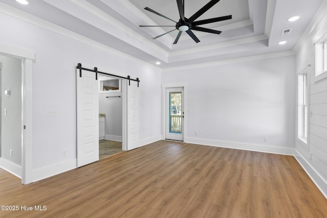 unfurnished bedroom with hardwood / wood-style flooring, crown molding, a tray ceiling, and a barn door