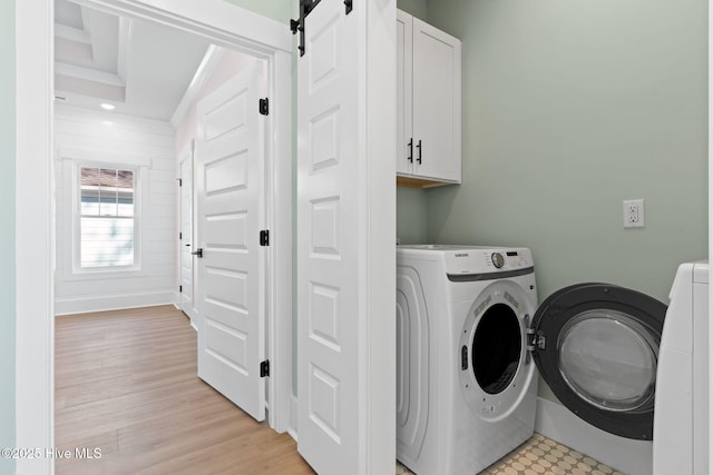 clothes washing area featuring light hardwood / wood-style flooring, a barn door, cabinets, and independent washer and dryer