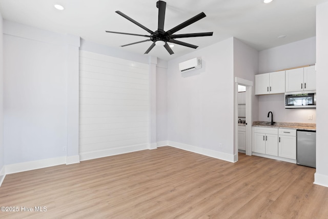 unfurnished living room with ceiling fan, light wood-type flooring, sink, and an AC wall unit