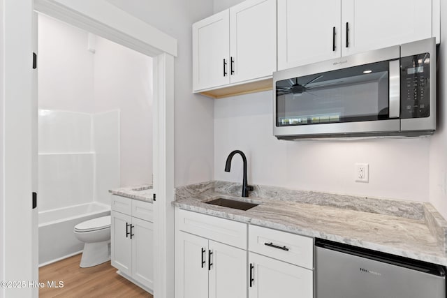 kitchen featuring sink, white cabinets, light hardwood / wood-style flooring, light stone countertops, and dishwashing machine