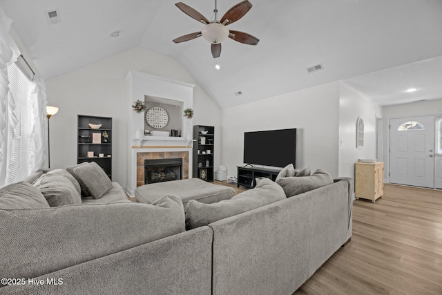 living room featuring ceiling fan, lofted ceiling, light hardwood / wood-style floors, and a tile fireplace