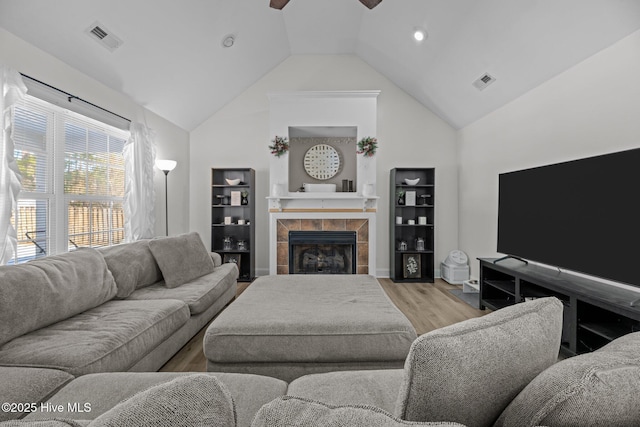 living room with a fireplace, vaulted ceiling, ceiling fan, and light wood-type flooring