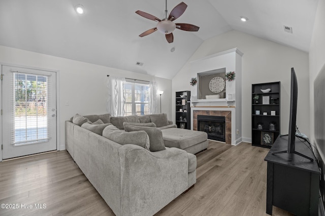 living room with lofted ceiling, a fireplace, ceiling fan, and light wood-type flooring