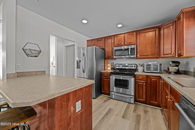 kitchen with sink, a breakfast bar area, light hardwood / wood-style flooring, appliances with stainless steel finishes, and kitchen peninsula