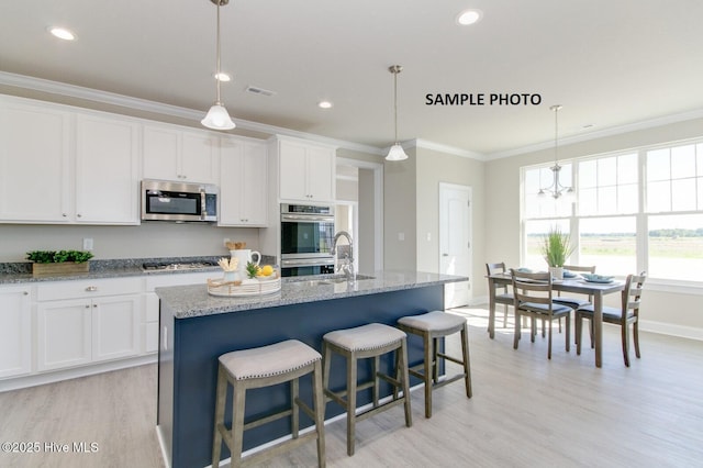 kitchen with a kitchen island with sink, white cabinets, stainless steel appliances, and decorative light fixtures