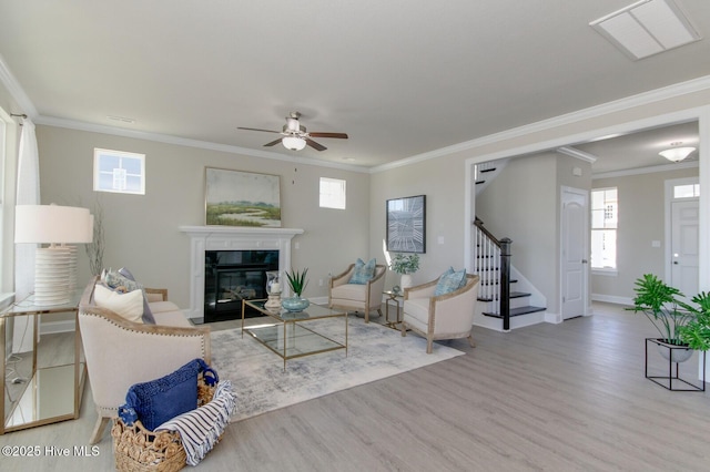 living room with a tile fireplace, a healthy amount of sunlight, light hardwood / wood-style floors, and ornamental molding