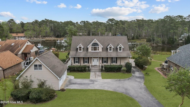 new england style home with covered porch, a front yard, and a water view