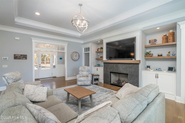 living room featuring dark hardwood / wood-style floors, crown molding, a tray ceiling, a premium fireplace, and an inviting chandelier