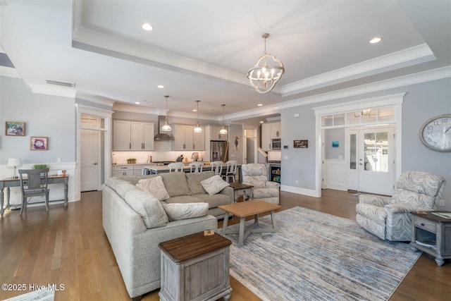 living room with an inviting chandelier, ornamental molding, a raised ceiling, and hardwood / wood-style flooring