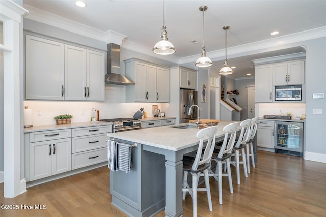 kitchen featuring wine cooler, wall chimney exhaust hood, light stone counters, decorative light fixtures, and a kitchen island with sink