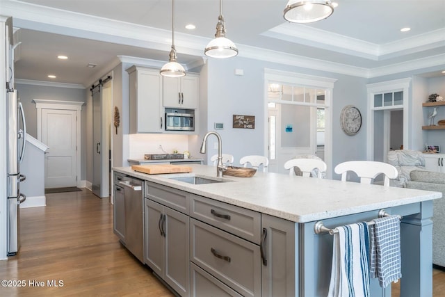 kitchen featuring sink, wood-type flooring, appliances with stainless steel finishes, an island with sink, and a barn door