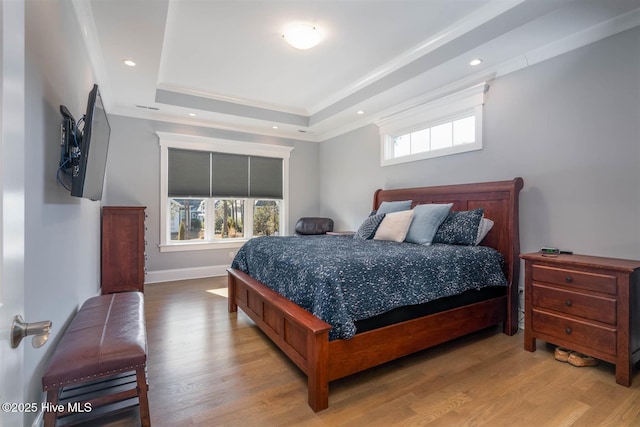 bedroom with crown molding, light wood-type flooring, and a tray ceiling