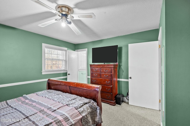 bedroom with ceiling fan, light colored carpet, and a textured ceiling