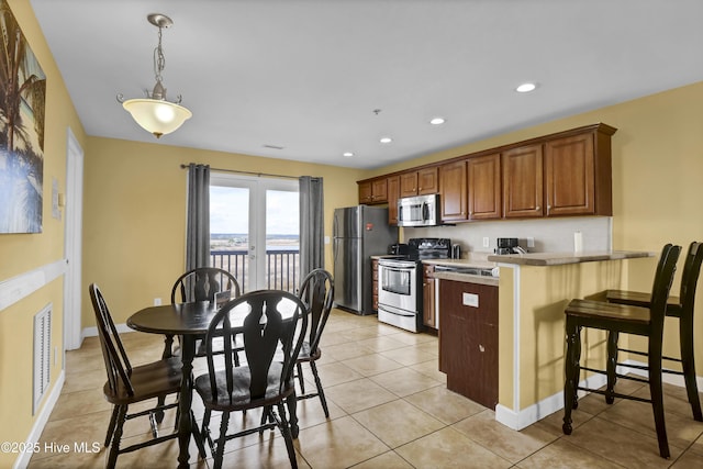 kitchen with kitchen peninsula, stainless steel appliances, hanging light fixtures, a breakfast bar area, and light tile patterned flooring