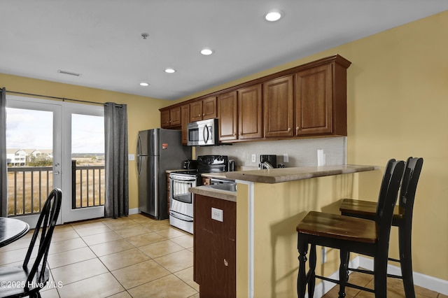 kitchen featuring french doors, kitchen peninsula, a breakfast bar area, light tile patterned floors, and appliances with stainless steel finishes