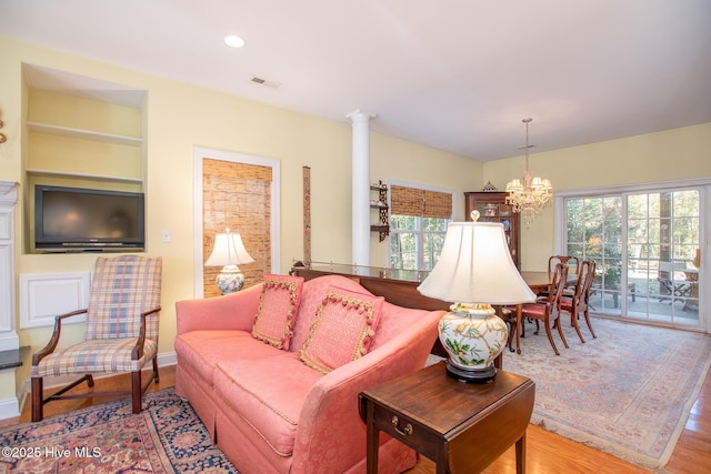 living room with built in features, decorative columns, an inviting chandelier, and light hardwood / wood-style flooring