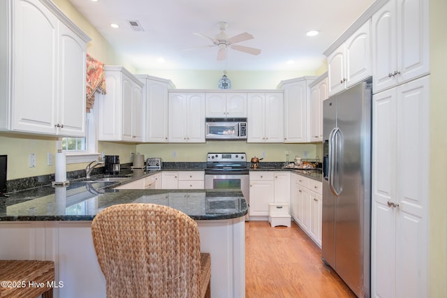 kitchen featuring appliances with stainless steel finishes, white cabinetry, light hardwood / wood-style floors, sink, and kitchen peninsula