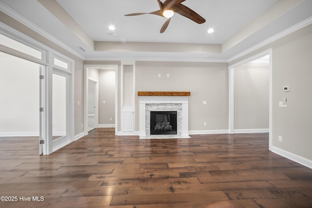 unfurnished living room featuring a tray ceiling, ceiling fan, dark wood-type flooring, and ornamental molding