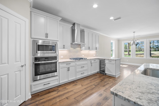 kitchen featuring light stone countertops, wall chimney exhaust hood, stainless steel appliances, beverage cooler, and white cabinets