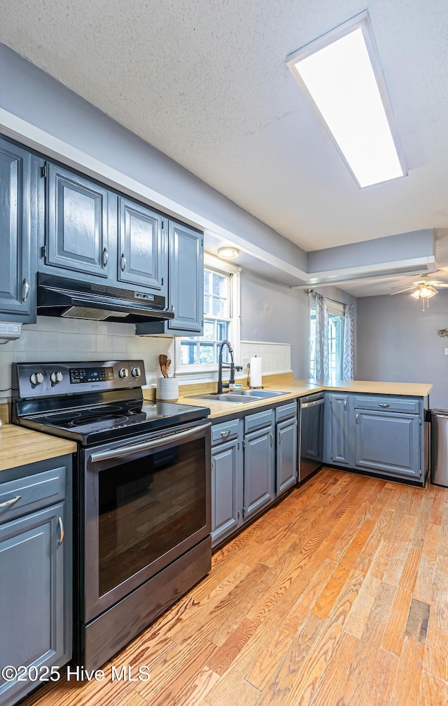 kitchen featuring light wood-type flooring, blue cabinetry, sink, tasteful backsplash, and appliances with stainless steel finishes