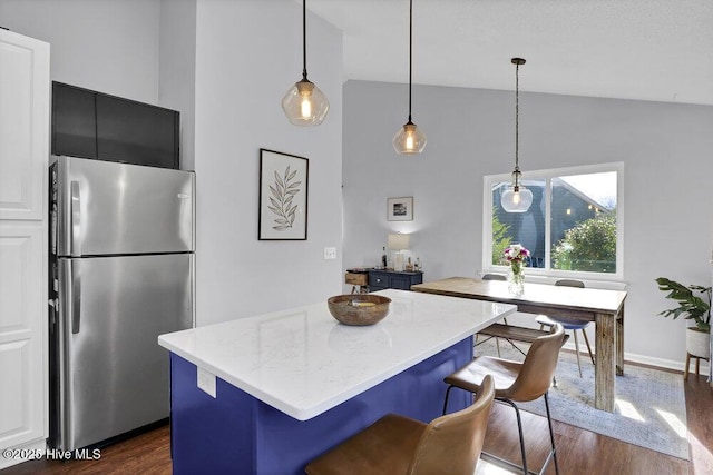 kitchen with dark wood-type flooring, decorative light fixtures, a center island, vaulted ceiling, and stainless steel fridge