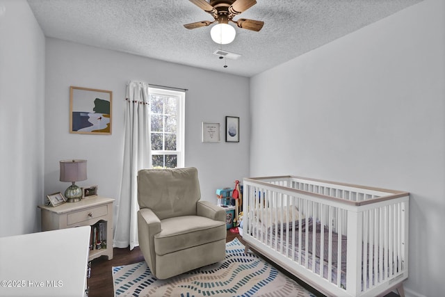 bedroom featuring a crib, ceiling fan, dark hardwood / wood-style floors, and a textured ceiling